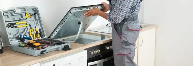 Cooktop repair technician lifting a built-in stovetop for service in Minneapolis, MN
