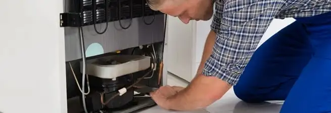 Refrigerator repair technician servicing the compressor and condenser area in Minneapolis, MN