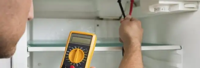 Refrigerator repair technician testing electrical components with a multimeter in Minneapolis, MN